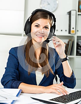 Office worker woman is working at a computer and talking by headset with client in the office