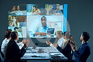 Office workers gather around conference table, engaged in online meeting with remote colleagues,looking project