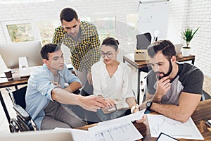 Office workers and a person in a wheelchair discuss working matters. They work in a bright office.