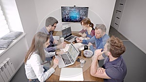 Office workers are sitting at table in meeting room and waiting a start of video conference with boss