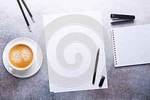 Office workplace with blank paper, cup of coffee, note pad and pen. Stone background. Top view