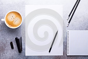 Office workplace with blank paper, cup of coffee, note pad and pen. Stone background. Top view