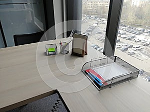 Office workplace in front of a large window. A table on which are notebooks, writing materials and other stationery