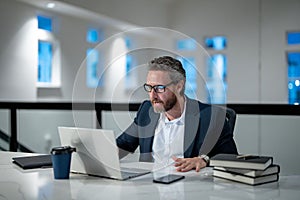 Office workplace. Handsome business man working with laptop at desk in office. Businessman typing on keyboard, online