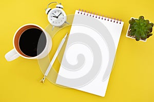 Office workplace minimal concept. Blank notebook with coffee, cactus, alarm clock and pencil on yellow background.