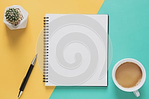 Office workplace minimal concept. Blank notebook with cup of coffee, cactus, pencil on yellow and blue background.