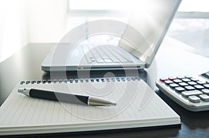 Office workplace with pen, notebook, calculator and computer lap