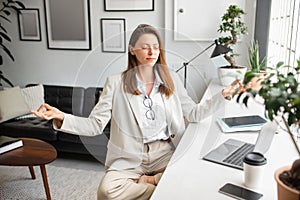 Office zen. Calm european businesswoman meditating with closed eyes in lotus position, feeling peaceful and balanced