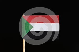 A official flag of Sudan on toothpick on black background. Flag consists of a horizontal red, white, black tricolour with a green