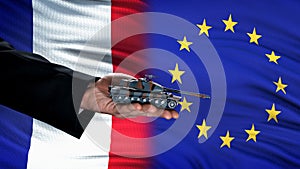 Official hand holding toy tank against France and EU flag, military pact