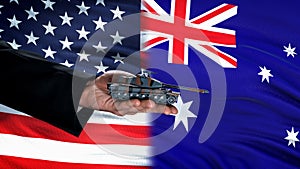 Official hand holding toy tank against USA and Australia flag, weapon trade