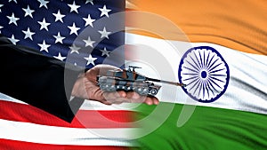 Official hand holding toy tank against USA and India flag background war concept