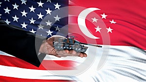 Official hand holding toy tank against USA and Singapore flag, protection