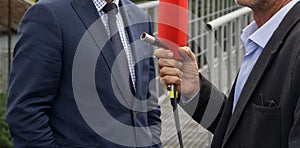 An official man in a jacket gives an interview to a TV journalist with a red microphone on the street. Unrecognizable. Photo.