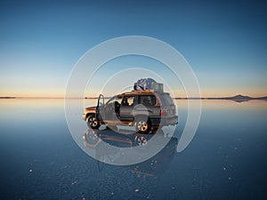 Offroad car SUV jeep of tour group on Salar de Uyuni salt flat lake in Bolivia andes mountains sunrise mirror reflection