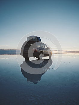 Offroad car SUV jeep of tour group on Salar de Uyuni salt flat lake in Bolivia andes mountains sunrise mirror reflection