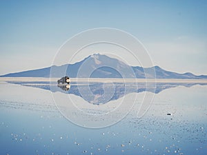 Offroad car SUV jeep of tour group on Salar de Uyuni salt flat lake in Bolivia andes mountains sunrise mirror reflection