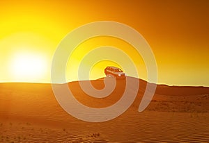 Offroad truck or suv riding dune in arabian desert at sunset. Offroad has been modified to be unrecognized. photo