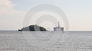 Offshore oil platform drilling site or oil rig project seen far in the middle of the sea and an island