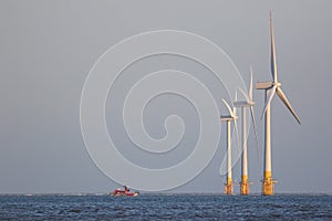 Offshore wind farm turbines on sea horizon with maintenance boat