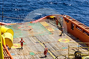 Offshore workers or riggers assisting placement of anchor buoy on deck of an anchor handling tug boat