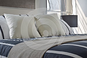 Offwhite and striped pillows on bed with deep blue striped blanket in modern interior style bedroom photo