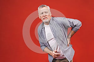 Oh, i need a massage! Portrait of a senior aged man having a back pain against a red background