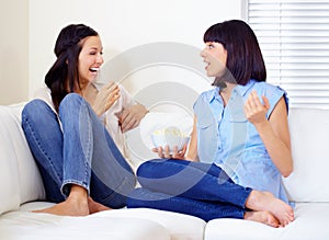 Oh my gosh. Two women having a good chat together with their feet up on a couch at home.