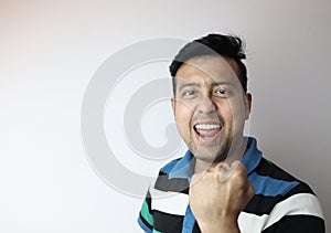 Oh yeah. face of an asian man with clinched fist showing delighted expression with a copy space with grey background photo