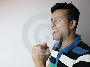 Oh yes. left side face of an asian man with clinched fist showing delighted expression looking towards a copy space with grey