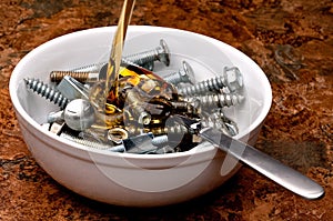 Oil being poured onto a bowl of nuts and bolts