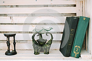 Oil burner , sand clock and old books lie on the white shelf