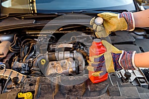 Oil change concept. Male hand in glove with oil bottle and car engine close up