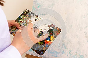 Oil color palette and female human hand holding brush, artist creative painting process. Woman drawing on canvas