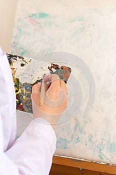 Oil color palette and female human hand holding brush, artist creative painting process. Woman drawing on canvas