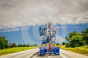 Oil drilling rig on truck driving on two lane ountry road - Overload sign on back - Room for copy