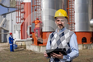 Oil Engineer With Digital Tablet Standing in front of Oil Refinery Storage Tanks