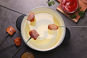 Oil in fondue pot, forks with fried meat pieces and sauces on grey table, flat lay