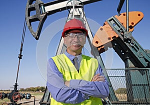 Oil and Gas Engineer in Red Hardhat and Yellow West Standing in front of the Oil Well Pump Jack