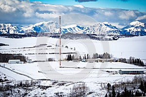 Oil and gas industry flare stack overlooking snow covered hills with Alberta Rocky Mountains at background in Western Canada