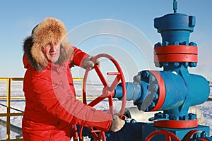 Oil and gas industry. A man in a red jacket opens a gas well to work