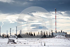 Oil and gas plant with a flare stack and flame under a dramatic winter sky in Western Canada
