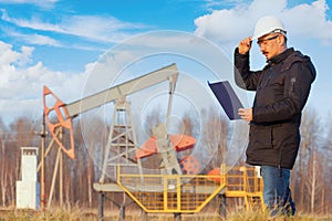 An oil geologist with a tablet next to an oil pump. Autumn
