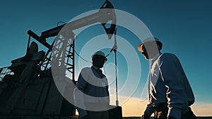 Oil industry, crude oil prices concept. Oilmen shaking hands next to an oil pump jack