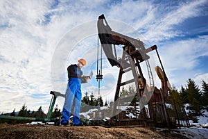 Oil man with laptop controlling work of pump jack.