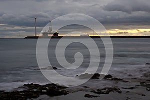 Oil platform and wind turbine at sunset.