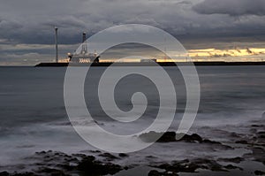 Oil platform and wind turbine at sunset.