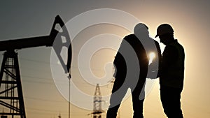 oil production. two silhouette workers work as a team next to an oil pump. business oil production production concept