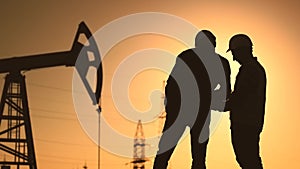 oil production. two silhouette workers work as a team next to an oil pump. business oil production production concept