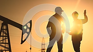 Oil production. Two silhouette workers work as a team next to an oil pump. Business oil production production concept